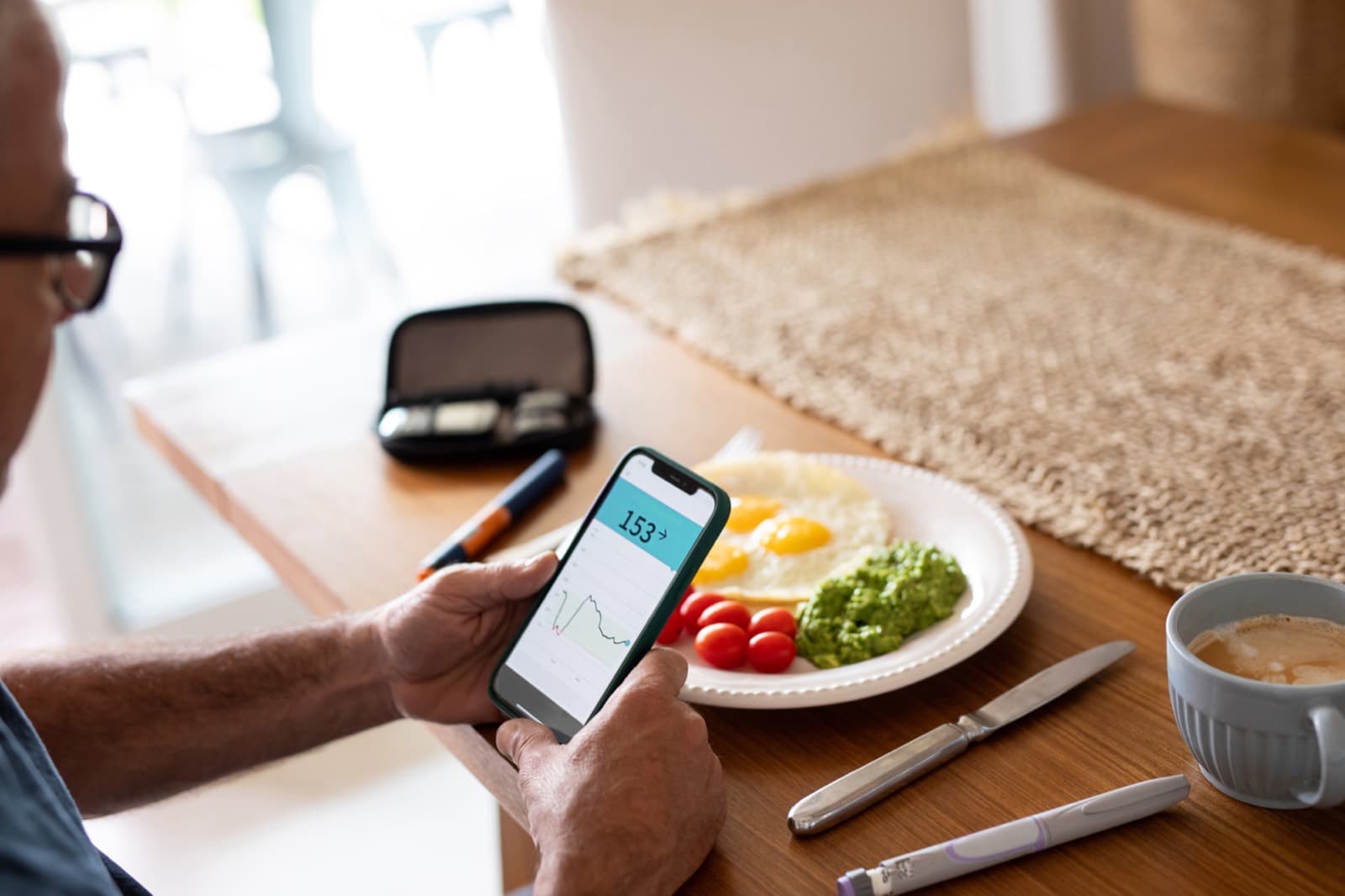 An older man checking his glucose readings on his phone over breakfast at home