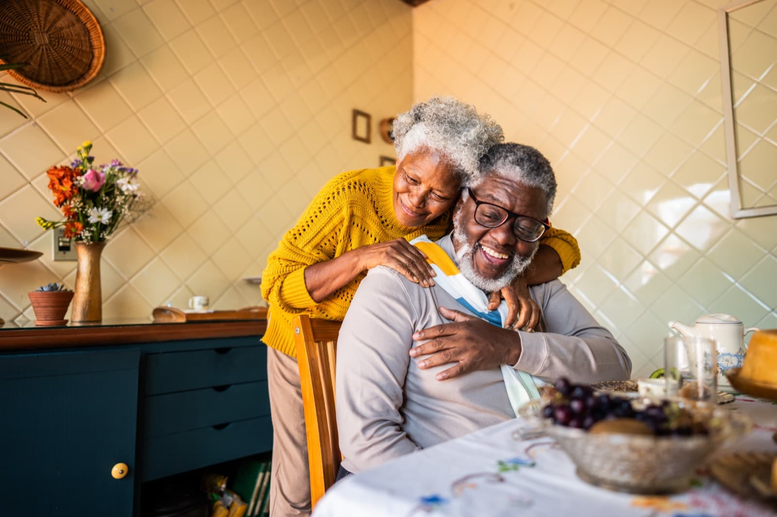 An older couple embracing and laughing together in their kitchen