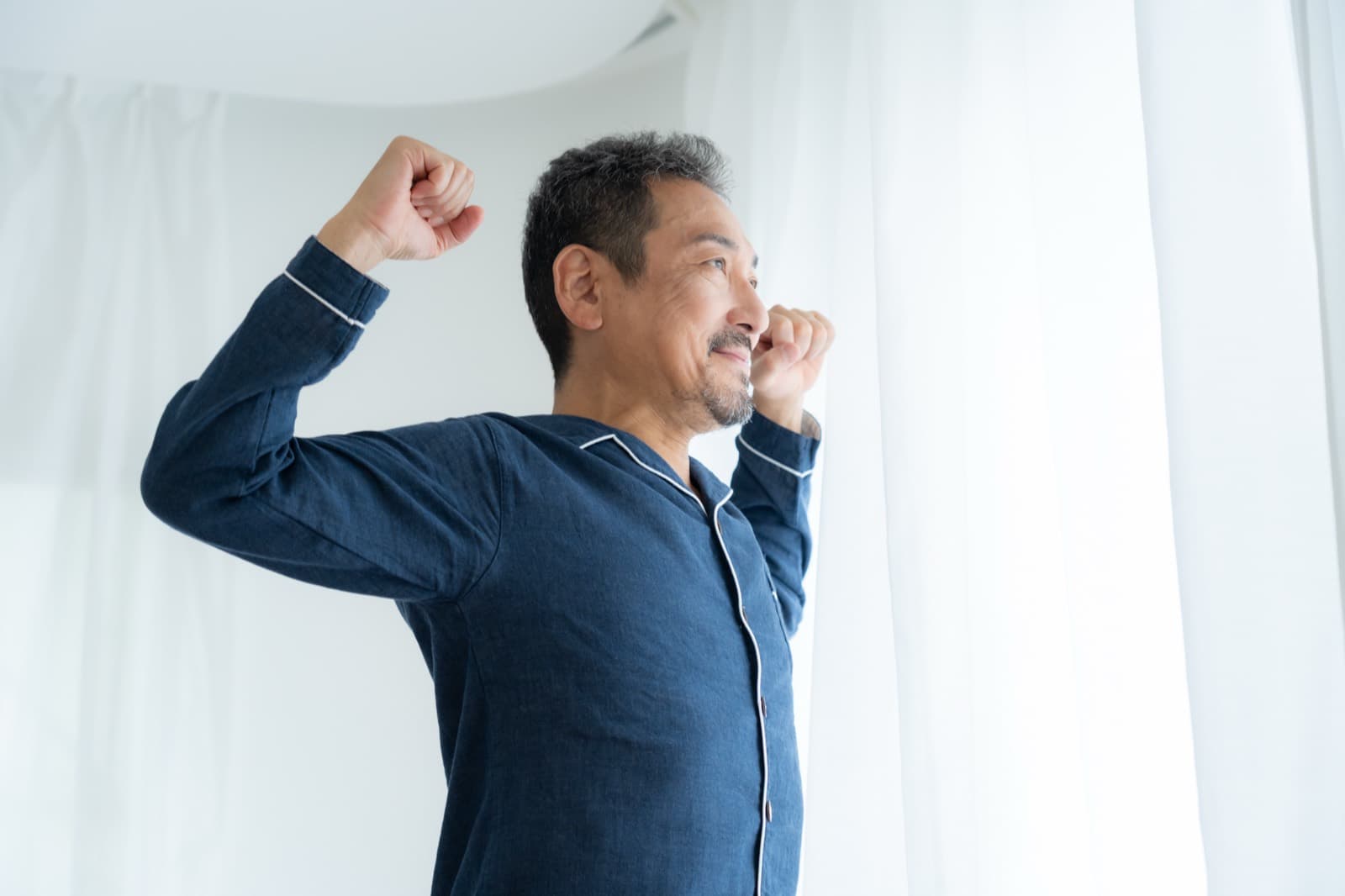 A man in pajamas stretching by the window, waking up rested