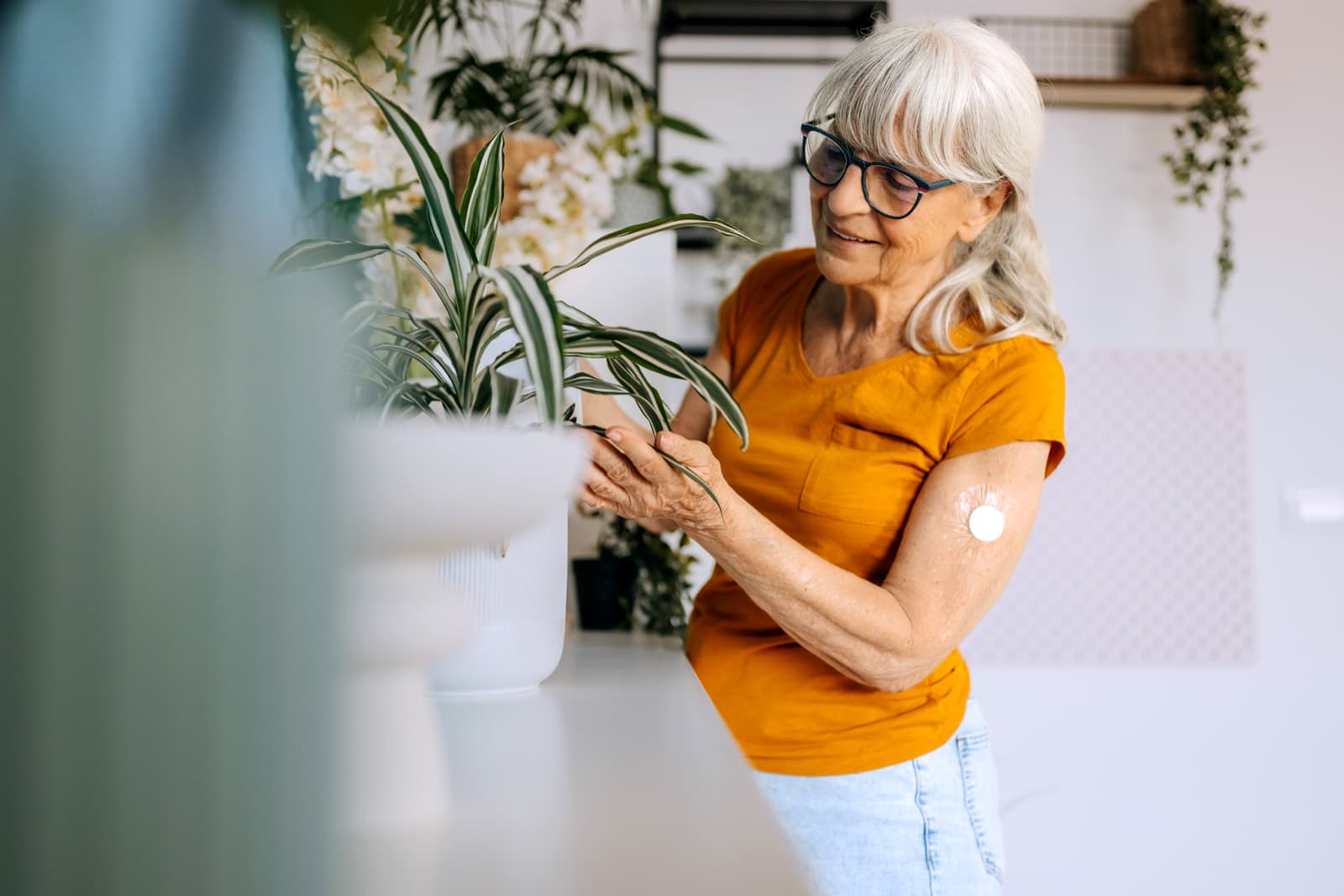An older woman tending her houseplants at home, a CGM sensor on her arm