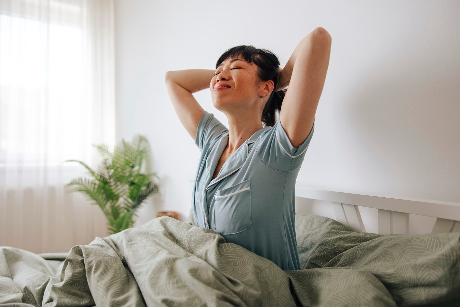 A woman stretching in bed after a full night's sleep, morning light through the window